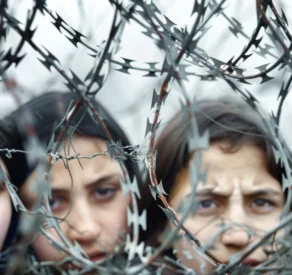 Close-up of distressed children behind a coil of razor wire, symbolizing conflict, displacement, and the harsh realities faced by refugees or victims of war.