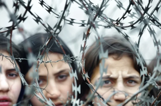 Advocating for Female Hostages in Gaza 1 Close-up of distressed children behind a coil of razor wire, symbolizing conflict, displacement, and the harsh realities faced by refugees or victims of war.